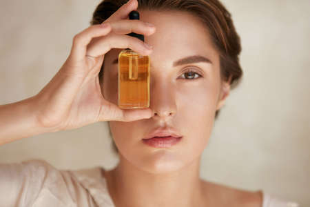Beauty Face. Close Up Portrait Of Woman With Bottle Of Essential Oil. Beautiful Model With Radiant And Glowing Facial Skin Looking At Camera. Moisturizing With Serum Collagen And Hyaluronic Acid.の写真素材