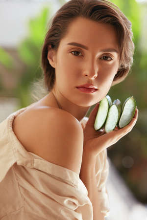 Beauty Face. Woman Holding Slices Of Aloe Vera Leaf And Looking At Camera. Tender Brunette With Naked Shoulder, Natural Makeup And Perfect Skin.の写真素材