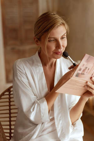 Makeup. Woman Using Cosmetic Brush For Applying Foundation Or Rouge. Beauty Portrait Of Female In Silk Pajama Having Morning Routine For Perfect Look.の写真素材