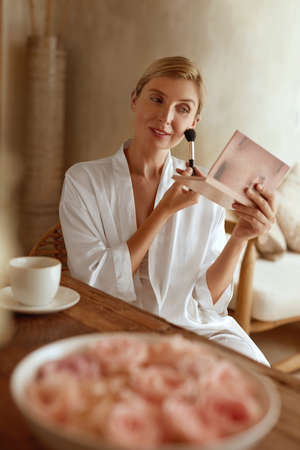 Woman Applying Makeup. Portrait Of Female Sitting In Bedroom And Using Cosmetic Brush. Lady In Silk Pajama Having Morning Beauty Routine.の写真素材