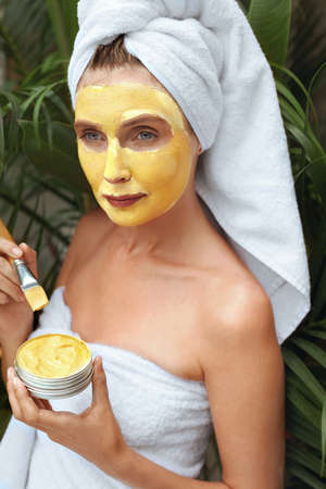 Skin Care. Woman With Yellow Clay Mask On Face. Female In Bath Towel With Brush For Applying Beauty Product With Turmeric. SPA Treatment And Anti-Aging Therapy For Perfect Facial Derma.の写真素材