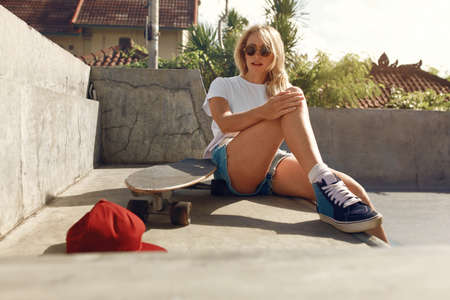Subculture. Skater Girl Sitting On Concrete Ramp At Skatepark. Teenager In Casual Outfit With Modern Sport Equipment Posing Outdoor. Urban Lifestyle For Active Teens In City.の写真素材