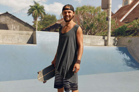 Subculture. Skater Man Against Concrete Ramp At Skatepark. Handsome Hipster In Casual Outfit With Modern Skateboard Posing Outdoor. Urban Lifestyle For Active Guys In City.の写真素材