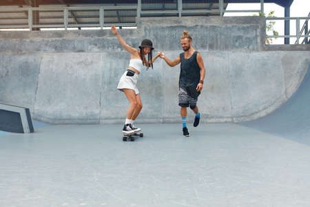 Couple At Skatepark. Happy Guy And Girl In Casual Outfit Riding On Skateboard. Extreme Sport And Skateboarding As Urban Subculture. Lifestyle Of Active People In City.の写真素材
