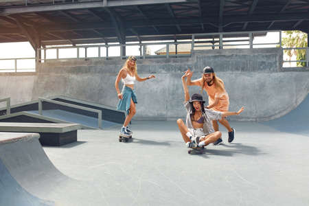 Skater Friends At Skatepark. Guy And Girls In Casual Outfit Riding On Skateboards. Summer Skateboarding With Modern Equipment As Part Of Active Lifestyle. Extreme Sport As Hobby.の写真素材