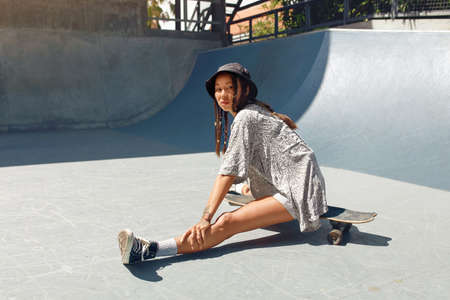 Summer. Skater Girl Sitting On Skateboard At Skatepark Portrait. Female Teenager In Casual Outfit Looking At Camera Against Concrete Wall. Urban Sport As Lifestyle Of Active Teens In City.の写真素材