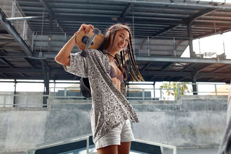 Subculture. Skater Girl With Skateboard At Skatepark Portrait. Asian Teenager In Casual Outfit With Modern Sport Equipment Against Skating Ramp. Urban Lifestyle For Active Teens In City.の写真素材