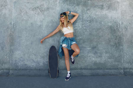Skater Girl At Skatepark. Full-Length Portrait Of Female Hipster In Casual Outfit With Skateboard Against Concrete Wall At Skate Park. Urban Subculture Style And Summer Sport In City. Active Lifestyle.の写真素材