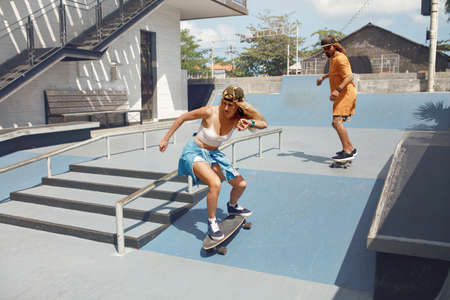 Skateboarding. Couple Riding On Skateboards At Skatepark. Skaters In Casual Outfit Doing Tricks On Concrete Ramp. Summer Activity As Lifestyle. Extreme Sport For Active Urban Guys And Girls.の写真素材