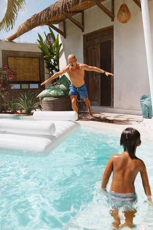 Summer Activity. Pool Entertainment With Kid On Vacation At Tropical Resort. Father Going To Jump On Floating Inflatable Water Mattress In Hot Weather. Fun Family Weekend As Lifestyle.の写真素材