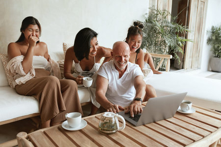 Happy Family With Laptop Having Fun Together. Dad, Mom And Daughters Sitting On Sofa In Patio,...