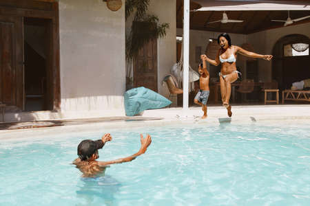 Pool. Mother And Son Jumping In Water From Poolside. Father Getting Ready To Catch Kid And Mom. Family Enjoying Vacation At Tropical Resort. Summer Activity As Lifestyle.の写真素材