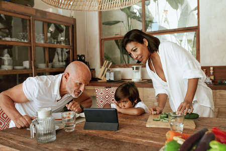 Family With Kid At Kitchen. Mother, Father And Son Using Tablet For Education At Home While Mom Cooks Organic Food. Healthy Vegetarian Diet As Lifestyle.の写真素材