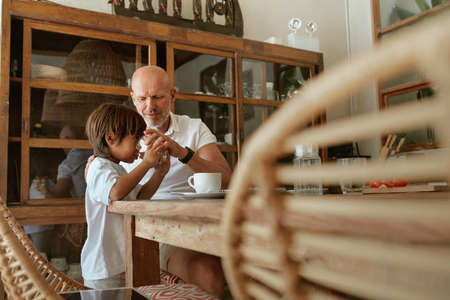 Boy Drinking Water. Father And Son Sitting At Wooden Table In Kitchen At Tropical Villa. Summer Vacation Or Family Weekend At Resort. Healthy Diet And Recovery As Lifestyle.の写真素材