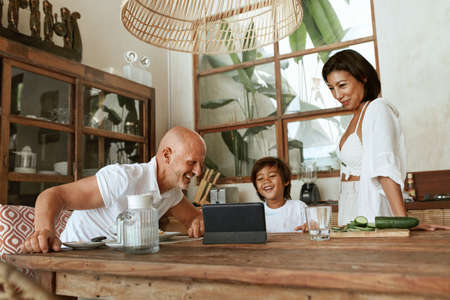 Family Cooking. Happy Parents With Kid Using Tablet At Kitchen Enjoying Weekend. Healthy Food. Positive Mother, Father And Son On Summer Vacation At Tropical Resort. Vegetarian Diet As Lifestyle.の写真素材