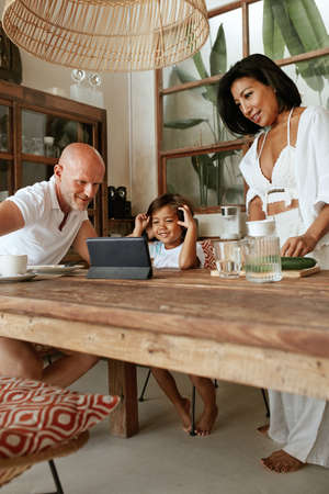Family At Kitchen. Father With Happy Son Using Tablet While Mother Cooking Healthy Food On Weekend. Parents And Kid Enjoying Summer Vacation At Tropical Resort. Digital Technology For Education.の写真素材