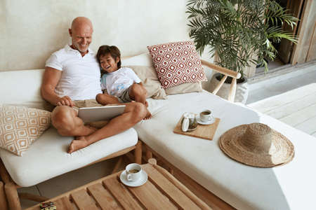 Family. Dad And Son With Tablet Resting In Tropical Villa Patio And Enjoying Weekend. Happy Father And Little Boy Having Fun With Digital Technology On Summer Vacation.の写真素材