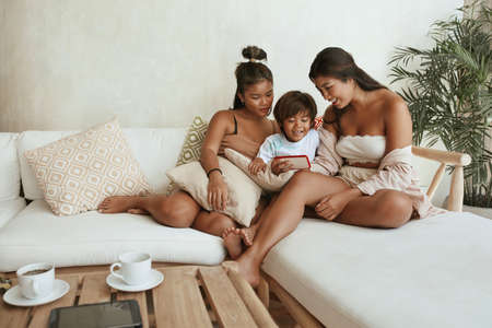 Siblings With Smartphone On Sofa. Group Of Different Age And Gender. Sisters And Brother Using Mobile Phone At Home And Enjoying Family Weekend. Summer Vacation At Tropical Resort.の写真素材