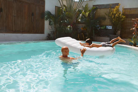 Summer Pool. Father And Son Enjoying Sunny Day. Little Boy Floating On Inflatable Water Mattress. Dad And Kid Enjoying Vacation At Tropical Resort. Family Weekend In Villa. Happiness As Lifestyle.の写真素材