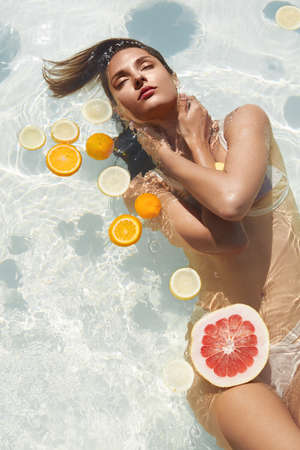 Beautiful Girl Floating With Citrus. Woman In Bikini Swimming In Pool At Tropical SPA Resort.の写真素材