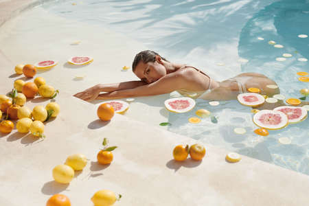 Summer Woman In Pool With Tropical Fruit Posing. Beautiful Model In Bikini At SPA.の写真素材