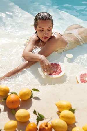 Beautiful Models Portrait In Pool With Citrus. Woman In Bikini Enjoying Fresh Exotic Fruit At SPA.の写真素材