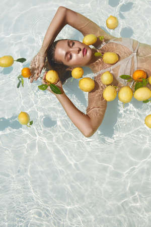 Models Portrait In Pool With Citrus. Beautiful Girl Floating On Water With Fresh Tropical Fruit At SPA.の写真素材