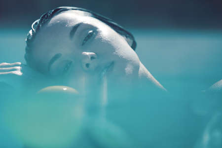 Beautiful Girl Face Portrait. Woman Floating In Pool At SPA And Looking At Camera.の写真素材