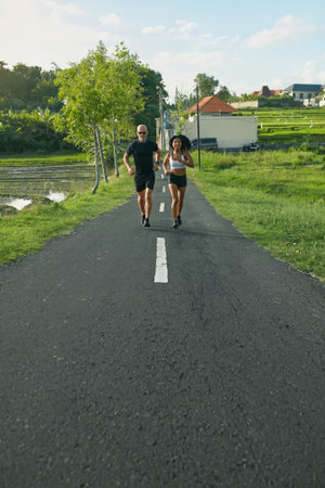 Mature Couple Running On Road At Tropical Landscape. Caucasian Man And Asian Woman On Jogging...