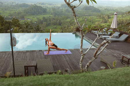 Beautiful Girl Doing Yoga On Poolside In Morning In Bali, Indonesia.の写真素材