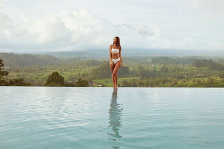 Beautiful Girl In Bikini In Infinity Pool Full-Length Portrait. Front View Of Young Woman With Sexy Body In Swimsuit.の写真素材