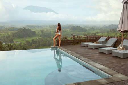 Beautiful Girl In Bikini In Infinity Pool Full-Length Portrait. Side View Of Young Woman With Sexy Body In Swimsuit.の写真素材