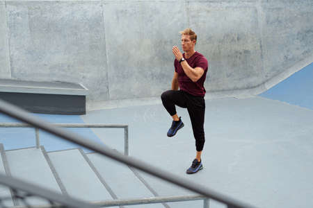 Young Man Running On Place Near Concrete Steps Outdoors. Handsome Caucasian Sportsman With Strong Muscular Body In Fashion Sportswear Warming Up Before Intense Workout.の写真素材