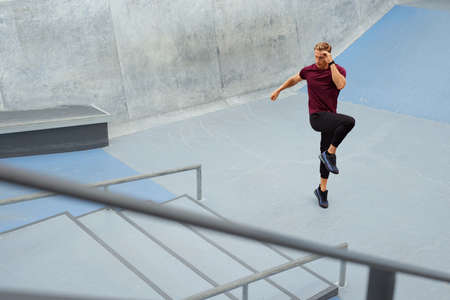 Young Man Running On Place Near Concrete Steps Outdoors. Handsome Caucasian Sportsman With Strong Muscular Body In Fashion Sportswear Warming Up Before Intense Workout.の写真素材