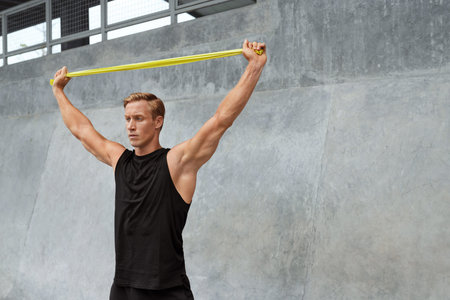 Young Man Stretching With Resistance Band Against Concrete Wall Outdoors. Handsome Caucasian...