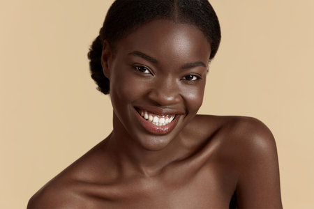 Portrait close up of beautiful african girl. Smiling young woman looking at camera. Concept of skincare. Isolated on beige background. Studio shootの写真素材