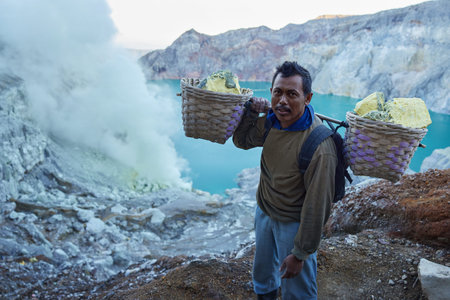 Java island, Indonesia - May 02, 2021: Indonesian man hold baskets with pieces of natural sulfur. Miner carrying sulfur on shoulders from crater mine. Sulphur mining operation in Kawah Ijen volcanoのeditorial素材
