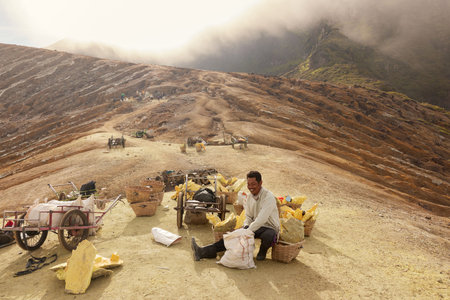 Java island, Indonesia - May 02, 2021: Indonesian miner collecting natural sulfur to bag near crater...