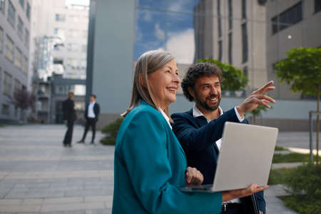 Positive Man Pointing Discussing with Colleague. Businesspeople Holding Laptopの写真素材