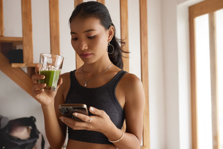 Calm Young Woman Holding Glass Of Fresh Smoothie In White Kitchen