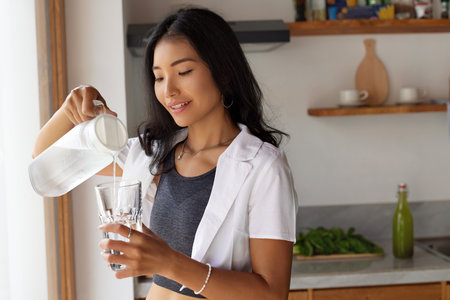 Drink Water. Happy Young Woman Pouring Glass Of Fresh Water In White Kitchenの写真素材
