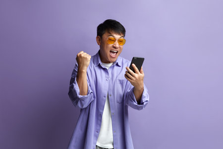 Winner Man Rejoicing Smartphone. Extremely Happy Asian Guy Raised Arm Gesturingの写真素材