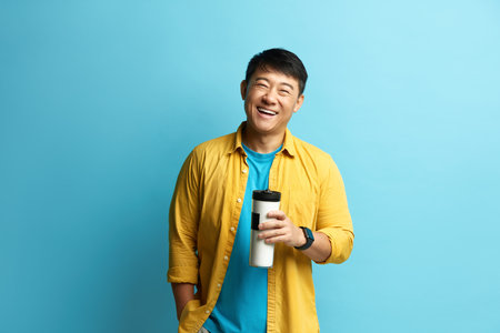 Smiling Man Holding Coffee. Portrait of Satisfied Asian Guy Holding Coffee to Goの写真素材