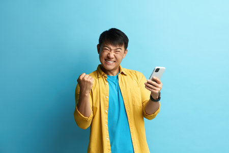 Winner Man Rejoicing Smartphone. Happy Asian Guy Raised Arm Gesturing Yesの写真素材