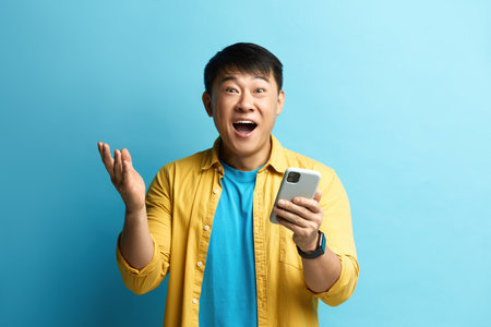 Winner Man Rejoicing Smartphone. Happy Asian Guy Raised Arm Gesturing Yesの写真素材