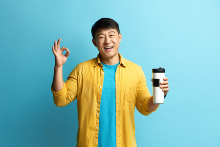 Smiling Man Showing Ok Gesture. Asian Guy Satisfied with Tasty Coffeeの写真素材