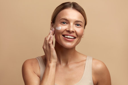 Skin Care Woman Applying Cream on Cheek. Beautiful Smiling Girl Putting Creamの写真素材