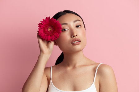 Skin Care Woman Posing with Red Flower. Asian Girl Holding Flower Looking Cameraの写真素材