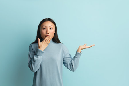 Surprised Woman Pointing Palm Away. Girl Hiding Mouth Gesturing at Empty Spaceの写真素材