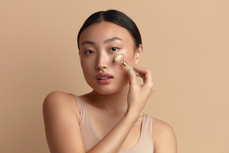 Face massage. Asian Woman Using Jade Facial Roller for Skin Careの写真素材